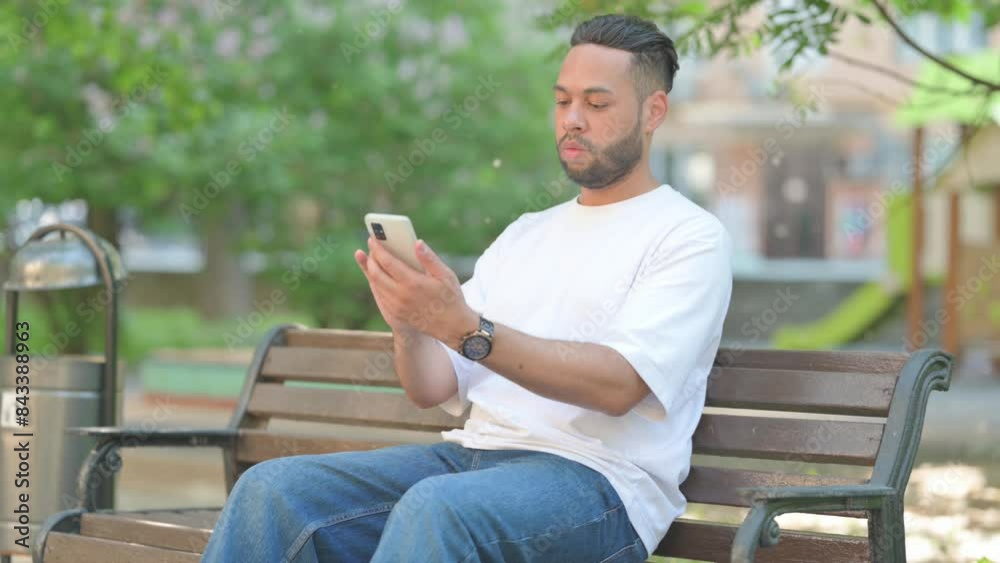 Young Man Using Smartphone while Sitting Outdoor on Bench