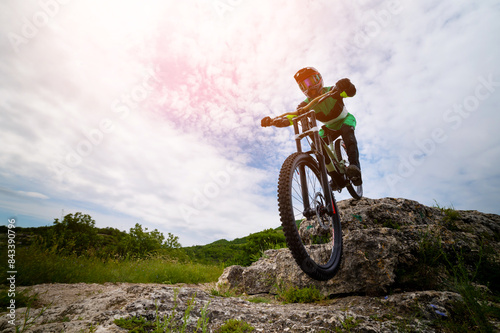 Cyclist riding a mountain bike down a cliff with beautiful countryside in the background. Extreme sport and enduro bike concept