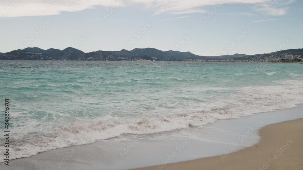 Slow motion Clear blue waves with strong wind on a sandy empty beach in Cannes with Theoule-sur-Mer on background Slow motion Clear blue waves with strong wind on a sandy empty beach in Cannes with Theoule-sur-Mer on background