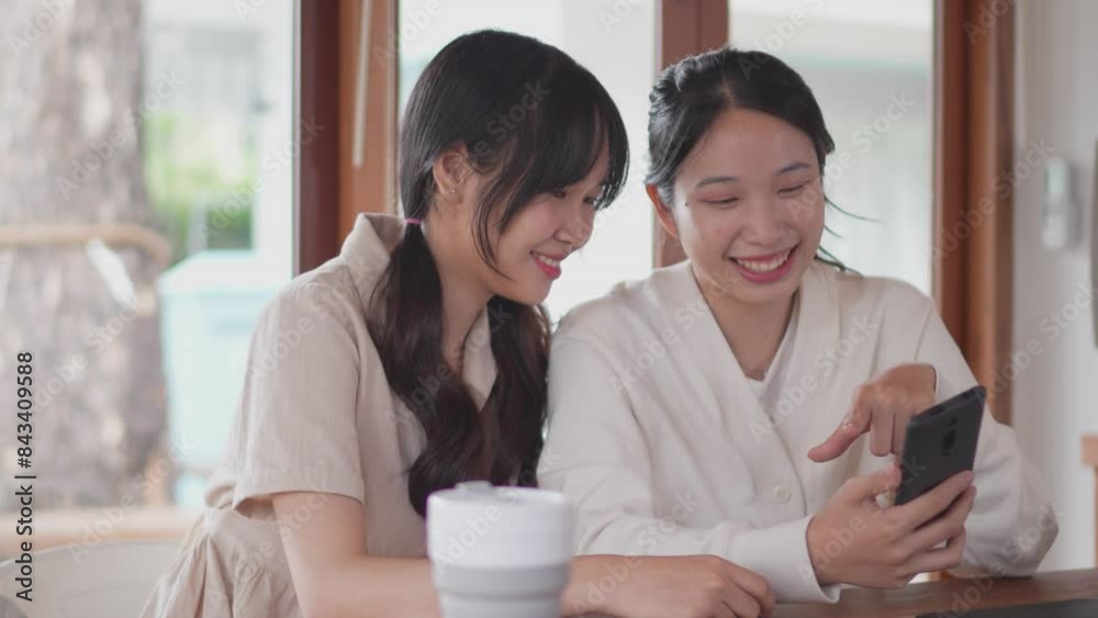 Two Asian university female friends are taking a break from studying, using a smartphone to browse social networks and capture good memories at their home Two Asian university female friends are taking a break from studying, using a smartphone to browse social networks and capture good memories at their home