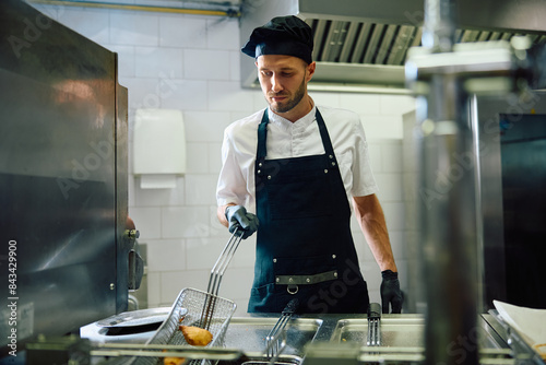 Male cook preparing food in deep fryer in  kitchen.