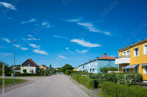 Wide street with colorful houses with green front gardens, blue sky on a summer day, Hallstahammar town, Sweden