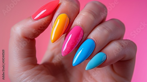 Closeup of hand with colorful almond-shaped nails against pink background.