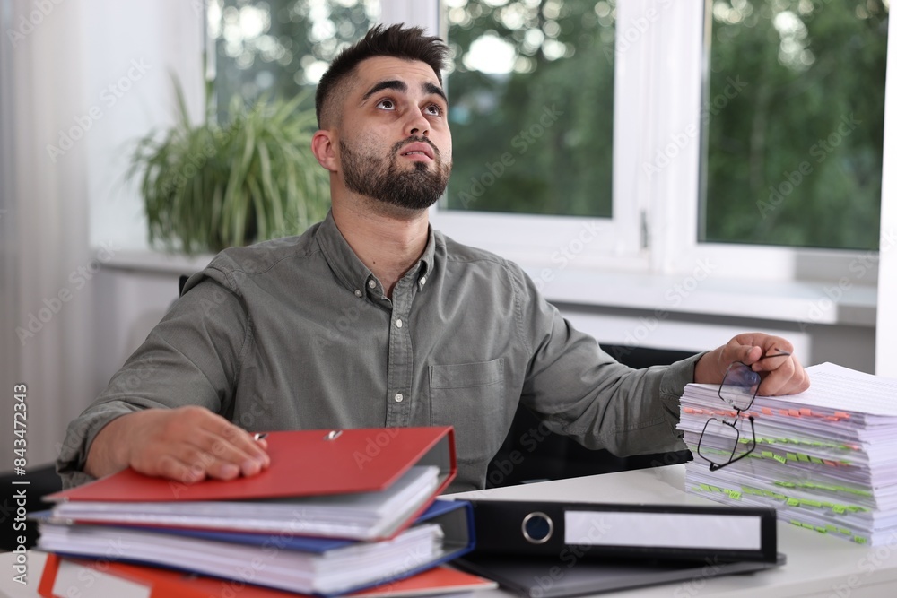 Naklejka premium Overwhelmed man sitting at table with documents in office