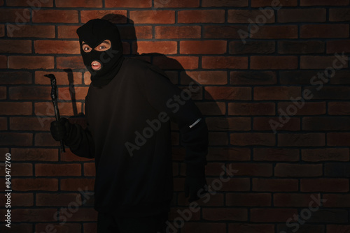 Thief in balaclava with crowbar against red brick wall