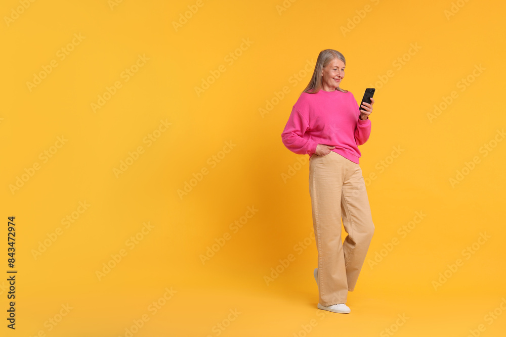 Senior woman with phone on orange background, space for text Senior woman with phone on orange background, space for text