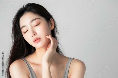 beautiful Korean woman her twenty long hair wearing grey tank top holding one hand side of her face if she gently touching She closed eye convey tranquility or focus something nearby background photo