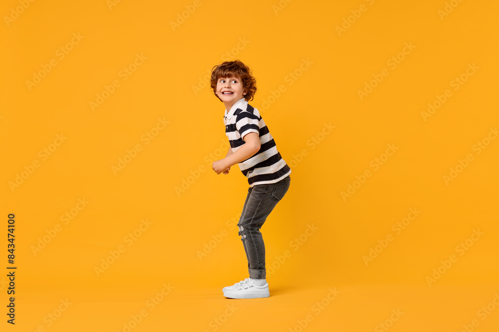 Fototapeta premium Happy little boy dancing on yellow background. Space for text