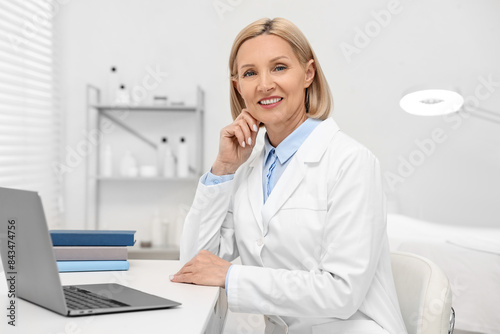 Portrait of happy dermatologist at white table in clinic