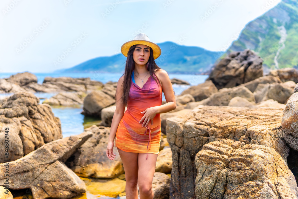 Naklejka premium A woman in a colorful dress stands in front of a rocky shoreline