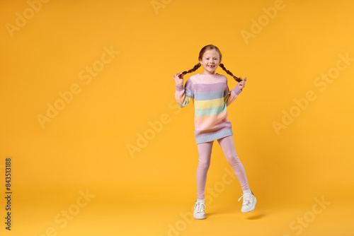 Cute little girl dancing on orange background, space for text