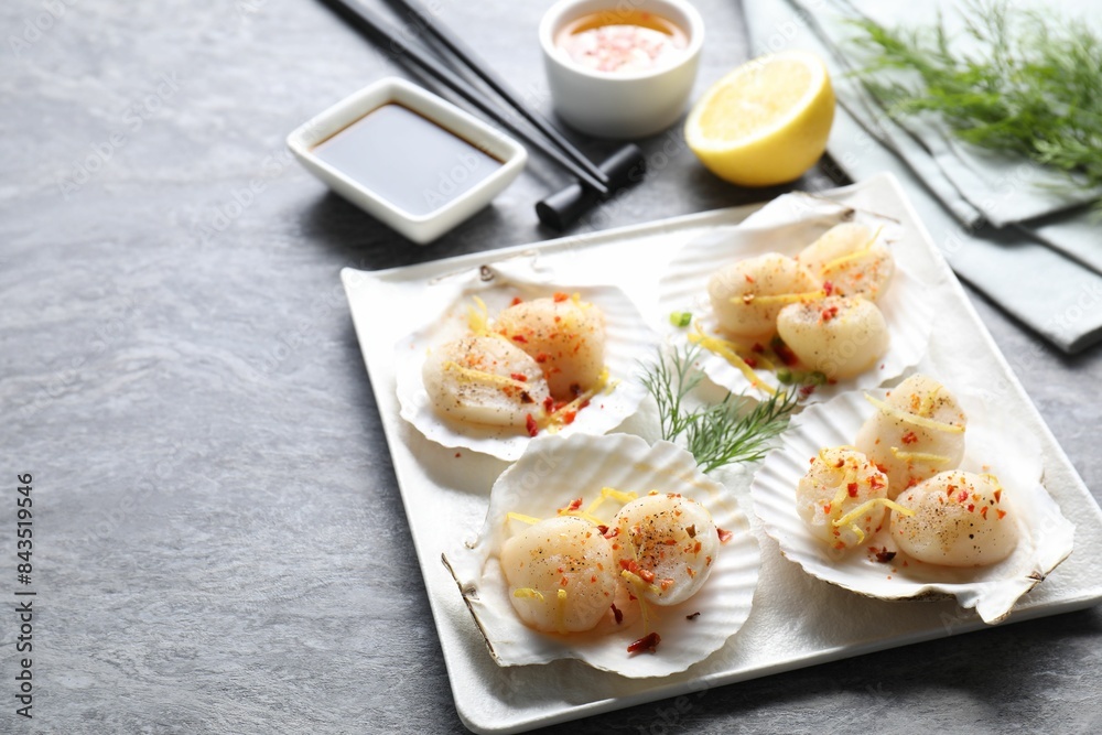 Raw scallops with spices, lemon zest and shells on grey marble table. Space for text Raw scallops with spices, lemon zest and shells on grey marble table. Space for text