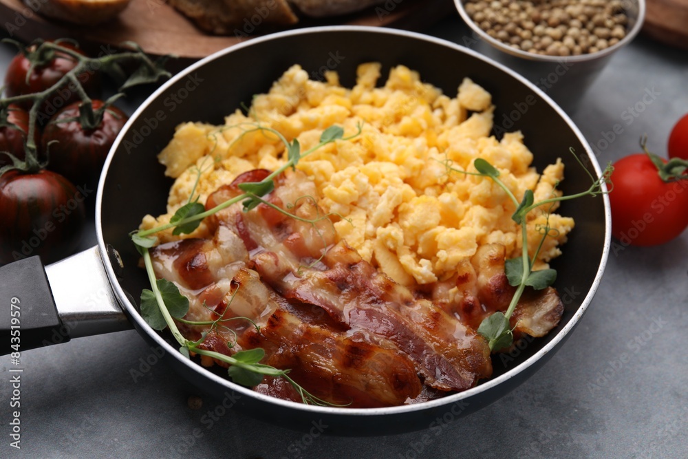 Fototapeta premium Delicious scrambled eggs with bacon in frying pan on grey table