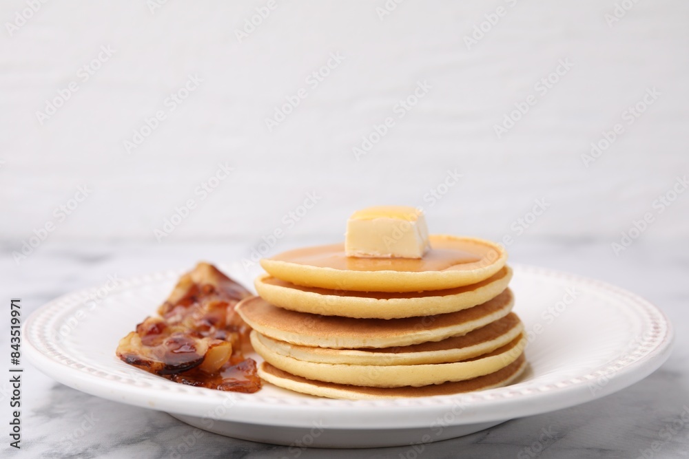 Delicious pancakes with butter, maple syrup and fried bacon on white marble table