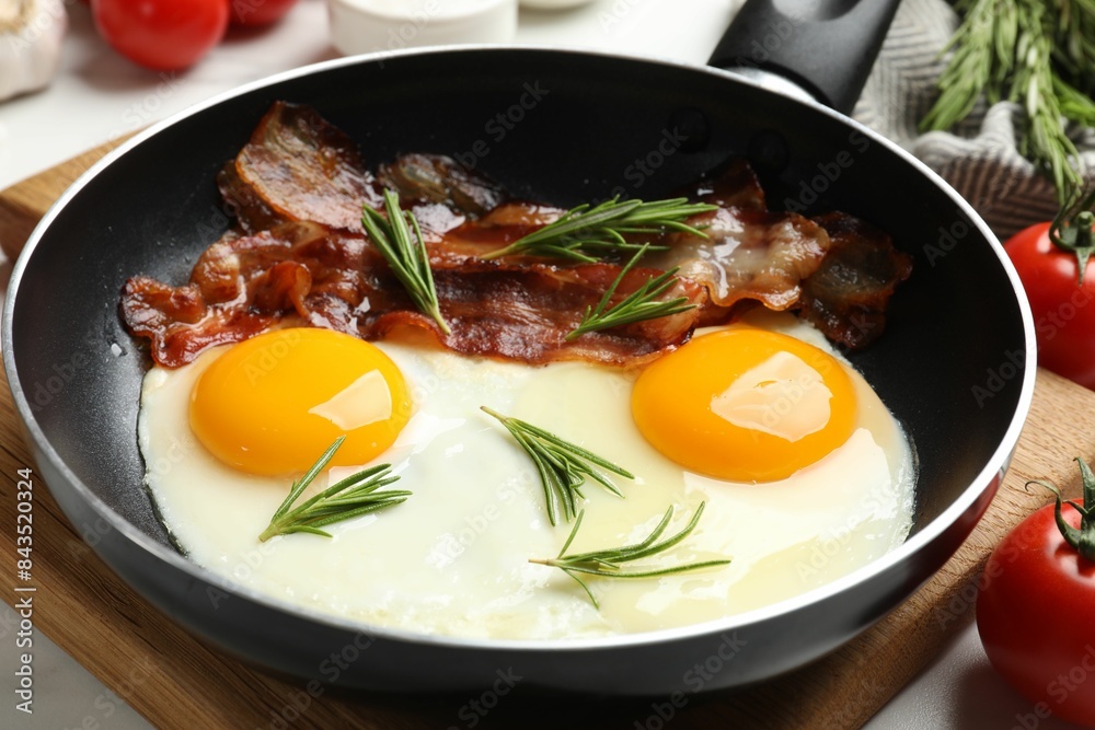 Tasty bacon, eggs and rosemary in frying pan on light table, closeup Tasty bacon, eggs and rosemary in frying pan on light table, closeup