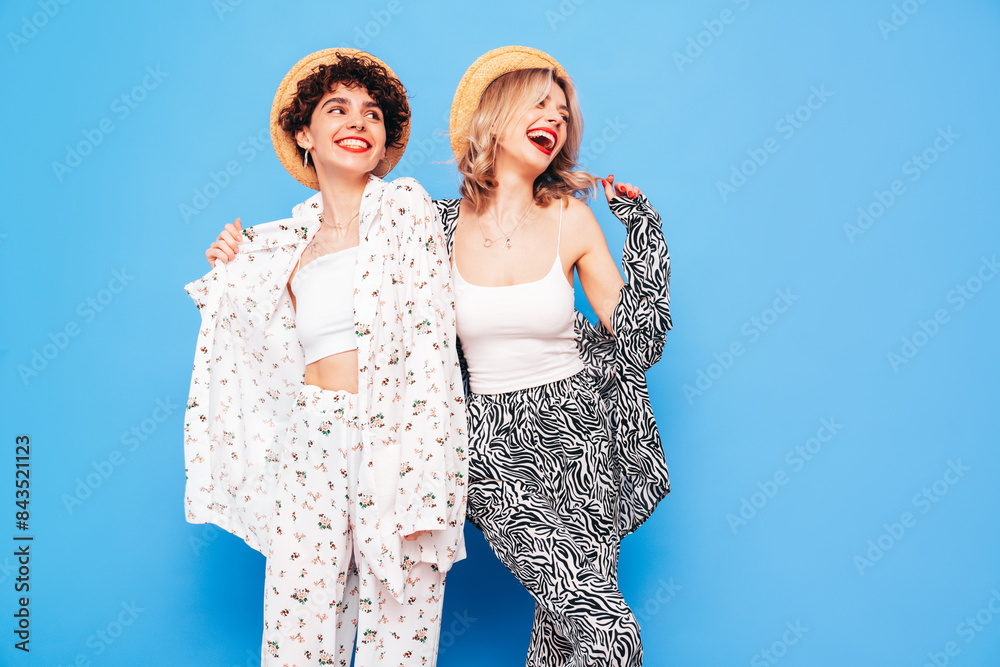 Two young beautiful smiling brunette hipster female in trendy summer costume clothes. Sexy women posing near blue wall in studio. Positive models having fun. Cheerful and happy
