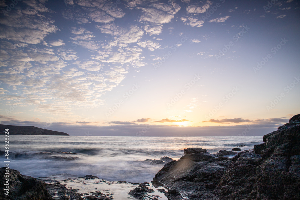 View of the sunrise over the Atlantic Ocean. Fantastic clouds and a bay with a stone beach on a volcanic island. Cold lava stones by the sea at Playa de Tarajalejo beach, Fuerteventura, Canary Islands View of the sunrise over the Atlantic Ocean. Fantastic clouds and a bay with a stone beach on a volcanic island. Cold lava stones by the sea at Playa de Tarajalejo beach, Fuerteventura, Canary Islands