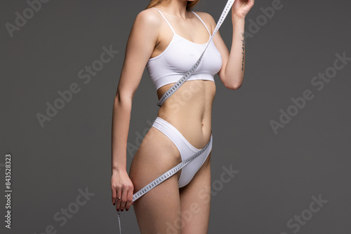 Athletic slim woman measuring her waist by measure tape after a diet over dark gray background.