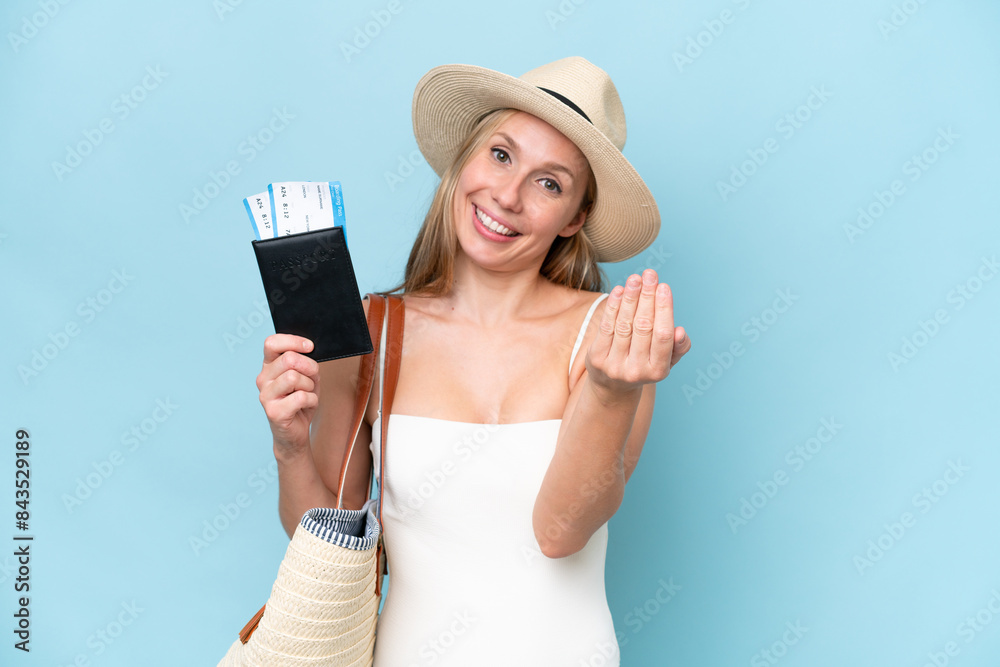Young blonde woman in swimsuit holding passport isolated on blue background inviting to come with hand. Happy that you came Young blonde woman in swimsuit holding passport isolated on blue background inviting to come with hand. Happy that you came