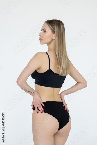 Young beautiful woman in black lingerie with a toned body and a slender figure on white background.