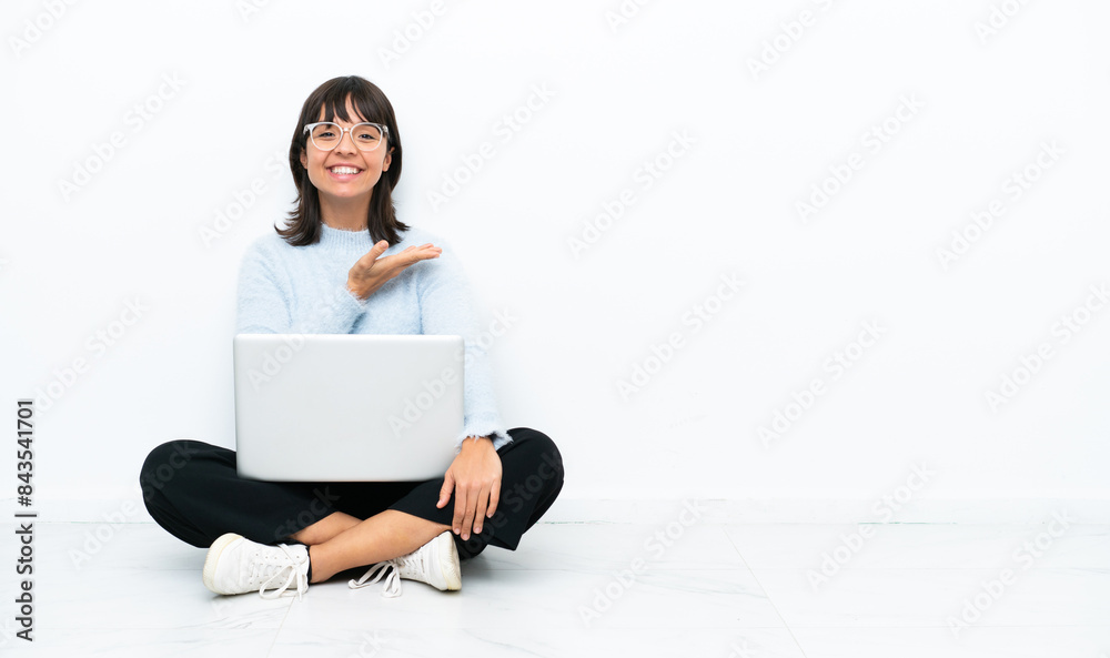 Young mixed race woman sitting on the floor with laptop isolated on white background presenting an idea while looking smiling towards Young mixed race woman sitting on the floor with laptop isolated on white background presenting an idea while looking smiling towards