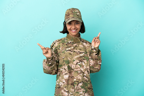 Military mixed race woman isolated on blue background pointing finger to the laterals and happy