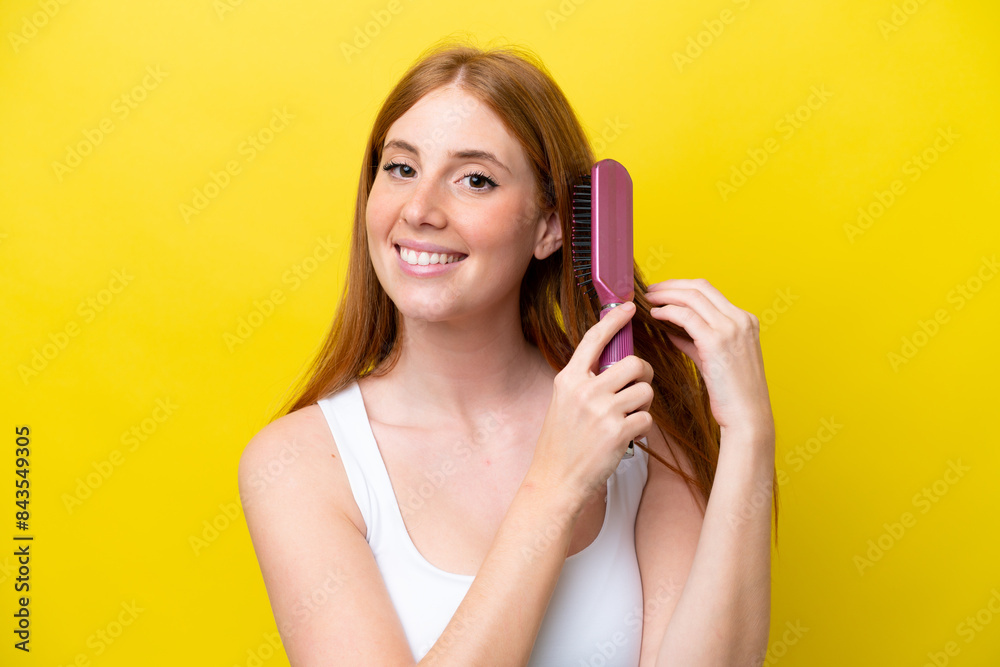 Young redhead woman isolated on yellow background with hair comb Young redhead woman isolated on yellow background with hair comb