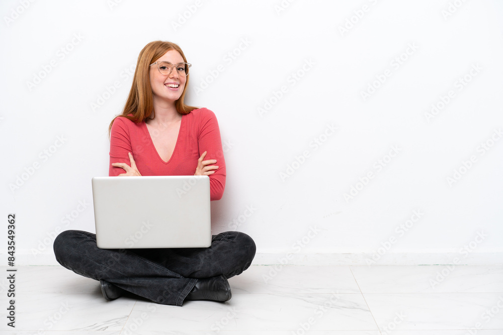 Young redhead woman with a laptop sitting on the floor isolated on white background with arms crossed and looking forward Young redhead woman with a laptop sitting on the floor isolated on white background with arms crossed and looking forward