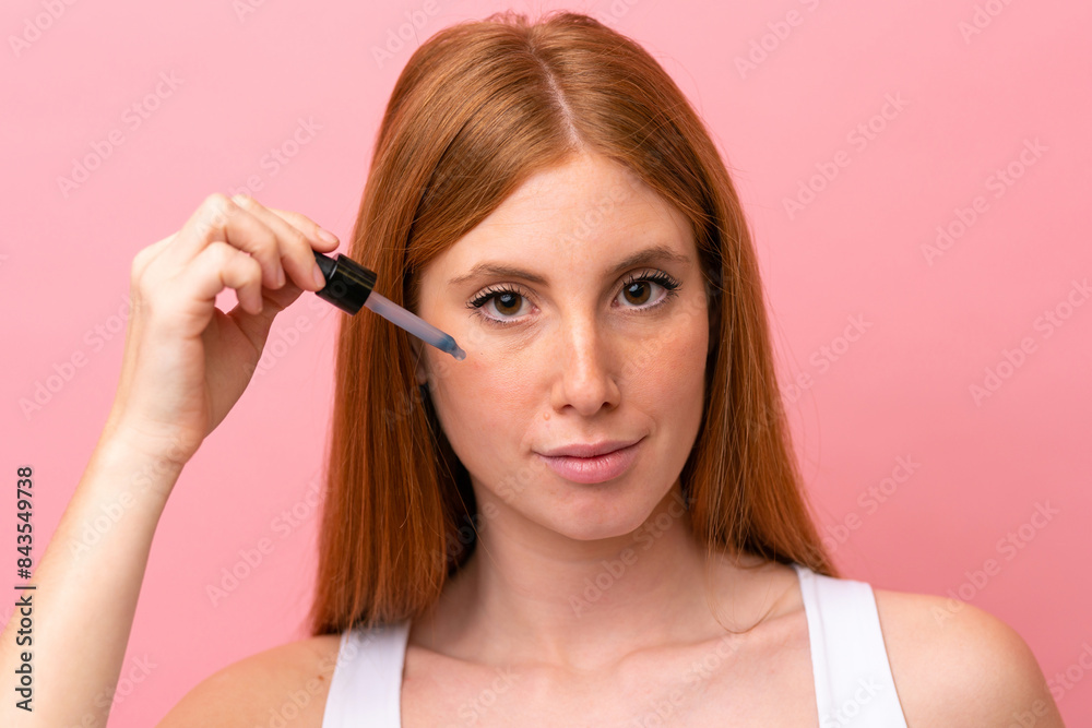 Young redhead woman isolated on pink background holding a serum. Close up portrait Young redhead woman isolated on pink background holding a serum. Close up portrait