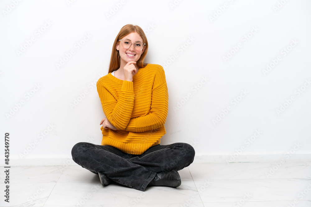 Young redhead woman sitting on the floor isolated on white background with glasses and smiling Young redhead woman sitting on the floor isolated on white background with glasses and smiling