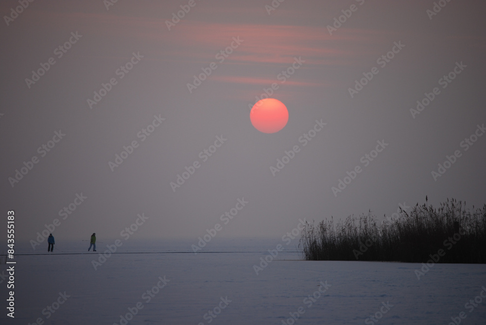 Sunset over the frozen and snow-covered lake in evening haze Sunset over the frozen and snow-covered lake in evening haze