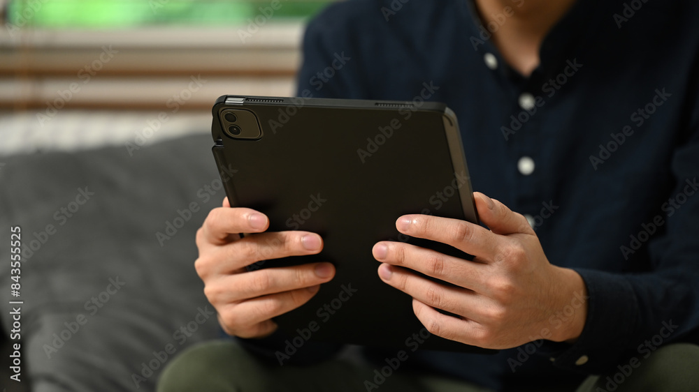 Cropped shot man watching video using digital tablet and relaxing on couch in living room Cropped shot man watching video using digital tablet and relaxing on couch in living room
