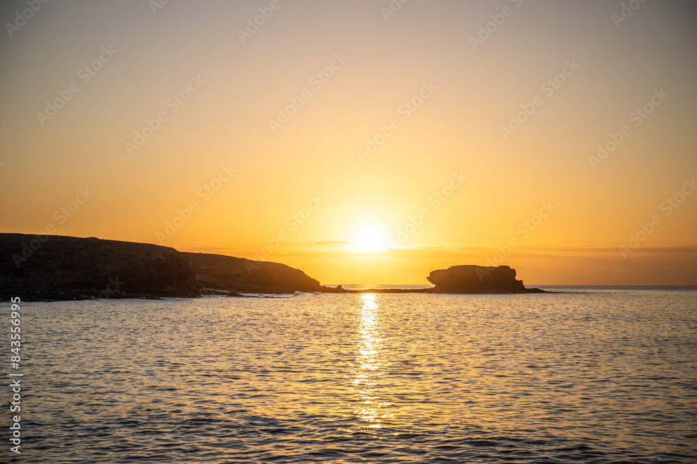 View of the sunrise over the Atlantic Ocean. View over a stone beach of a volcanic island. Cold lava stones by the sea on Playa Laja del Corral beach, Fuerteventura, Canary Islands, Spain View of the sunrise over the Atlantic Ocean. View over a stone beach of a volcanic island. Cold lava stones by the sea on Playa Laja del Corral beach, Fuerteventura, Canary Islands, Spain