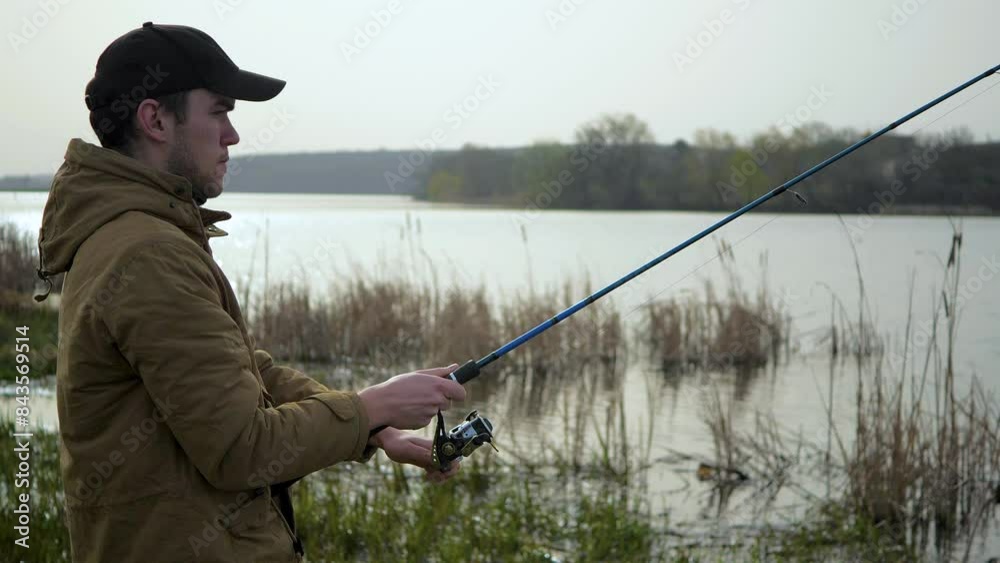 A young man is fishing on the river. Against the background of the blue sky, in nature, the fisherman watches the fish pecking and receives the pleasure of communicating with nature. A young man is fishing on the river. Against the background of the blue sky, in nature, the fisherman watches the fish pecking and receives the pleasure of communicating with nature.