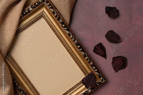 Empty frame with rose petals and fabric on a burgundy background from above. Vintage style. Top view