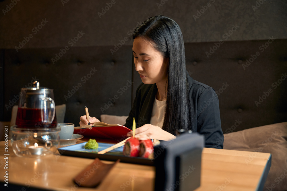 Creative young woman making notes in her notebook at japanese restaurant Creative young woman making notes in her notebook at japanese restaurant