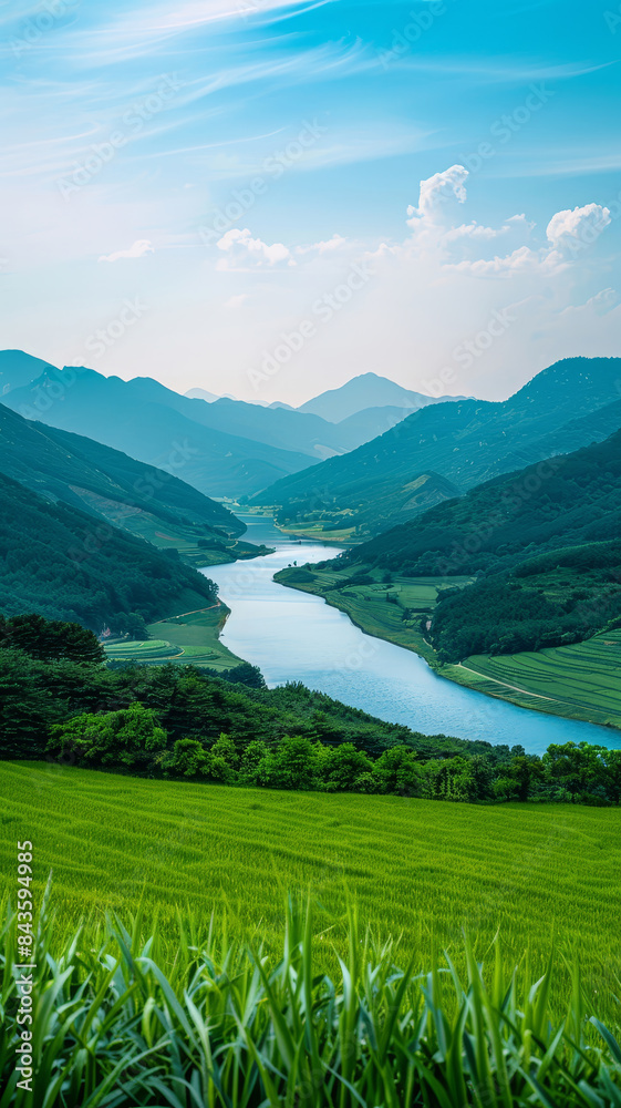 Serene river valley with lush green fields - This picturesque image shows a river winding through a valley, flanked by green hills with layers of mountains in the distance