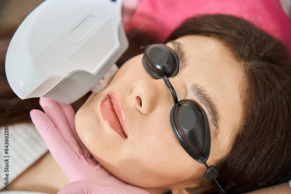 Female patient getting IPL photofacial carried out by esthetician