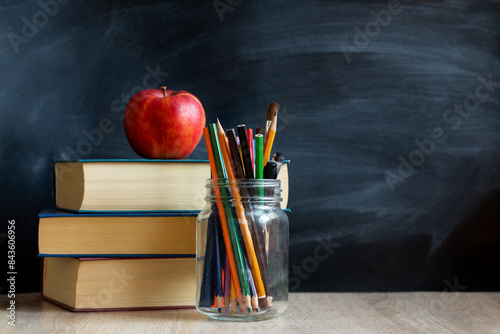 The concept of education, stack of books, an apple, pencils against the background of the school blackboard