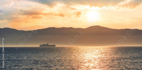 tropical seascape of sailing kargo tanker ship in sea with beautiful sunset and mountains on background