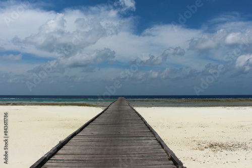 A long jetty, pier at the white sand beach coast of a tropical Maratua island in East Kalimantan on a bright sunny day with blue sky