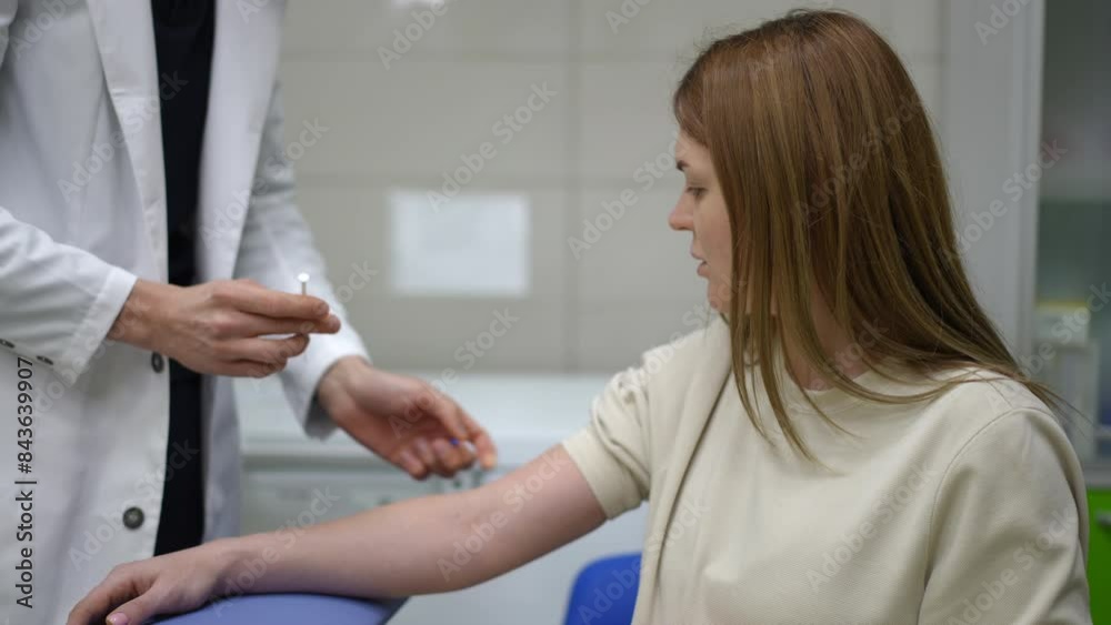Slow motion. An unrecognizable male physician uses a thin disposable syringe with a needle an injection into the forearm of a woman, who is sitting in the ambulance room. The doctor tapes the Slow motion. An unrecognizable male physician uses a thin disposable syringe with a needle an injection into the forearm of a woman, who is sitting in the ambulance room. The doctor tapes the