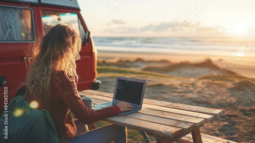 Fototapeta Naklejka Na Ścianę i Meble -  A female working on laptop by vintage camper van at sea beach in summer vacation