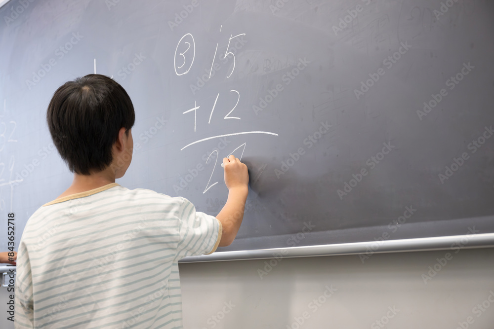 An elementary school student writing with chalk on the blackboard in math class