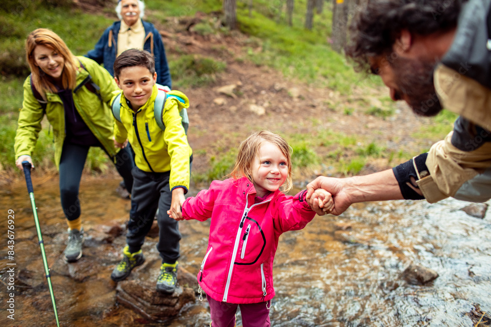 Multi-generational family crossing a stream during a forest hike Multi-generational family crossing a stream during a forest hike