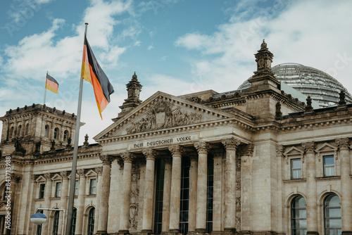 Mit Deutschlandflaggen beflaggter Reichstag in Berlin im Frühling vor blauem Himmel