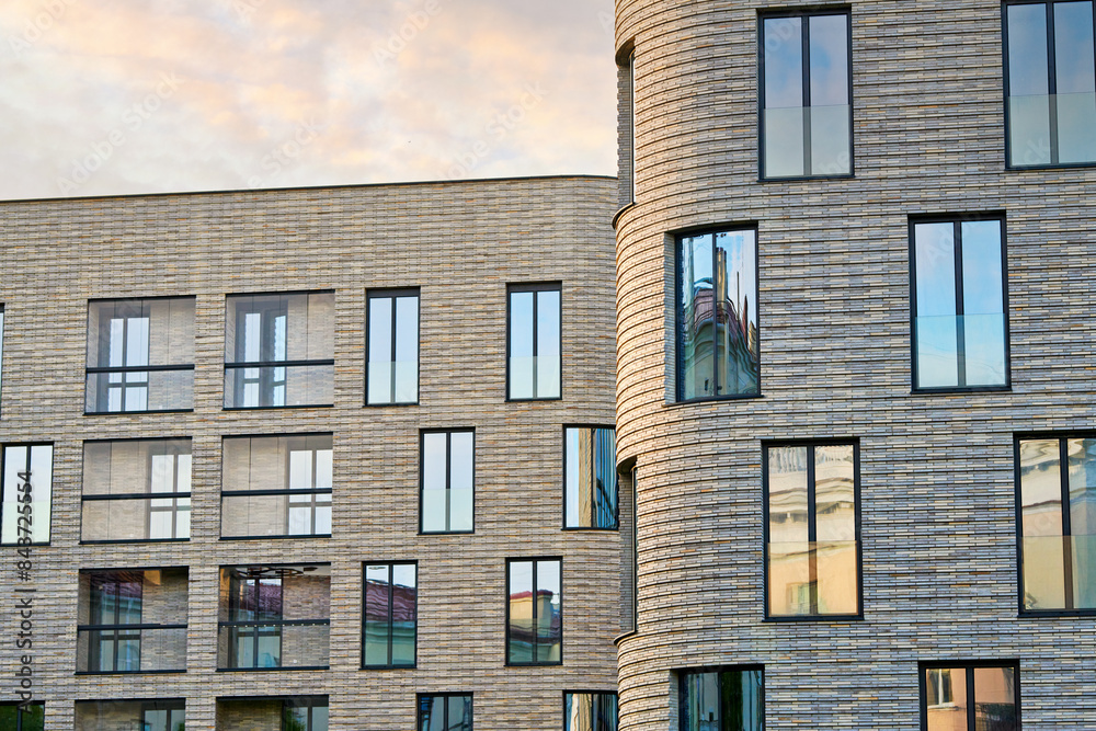 Modern residential building with large windows and clinker brick facade against susnet sky. Clinker brick facade and floor-to-ceiling glass windows Modern residential building with large windows and clinker brick facade against susnet sky. Clinker brick facade and floor-to-ceiling glass windows