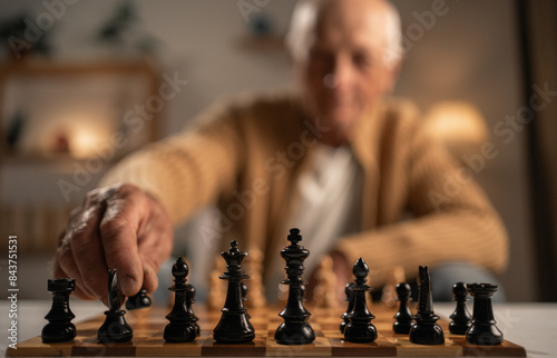 close-up of an elderly man playing chess, chessboard with pieces in the foreground and blurred background. Hobby and leisure photo