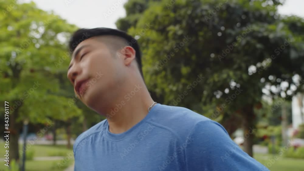 Tilt up of Asian male athlete stretching wrists and doing neck warm up after morning running in park Tilt up of Asian male athlete stretching wrists and doing neck warm up after morning running in park