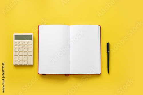 Financial objects - calculator and blank open page book on yellow background still life. Overhead view.